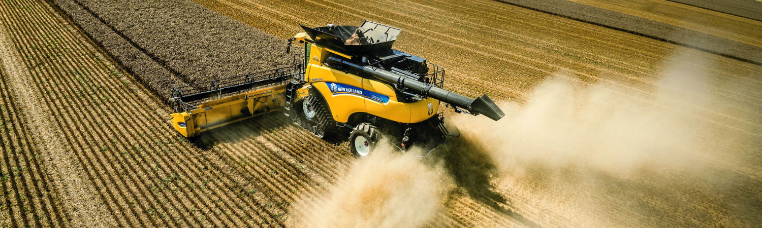 A New Holland baler that's driving through a field and picking up hay